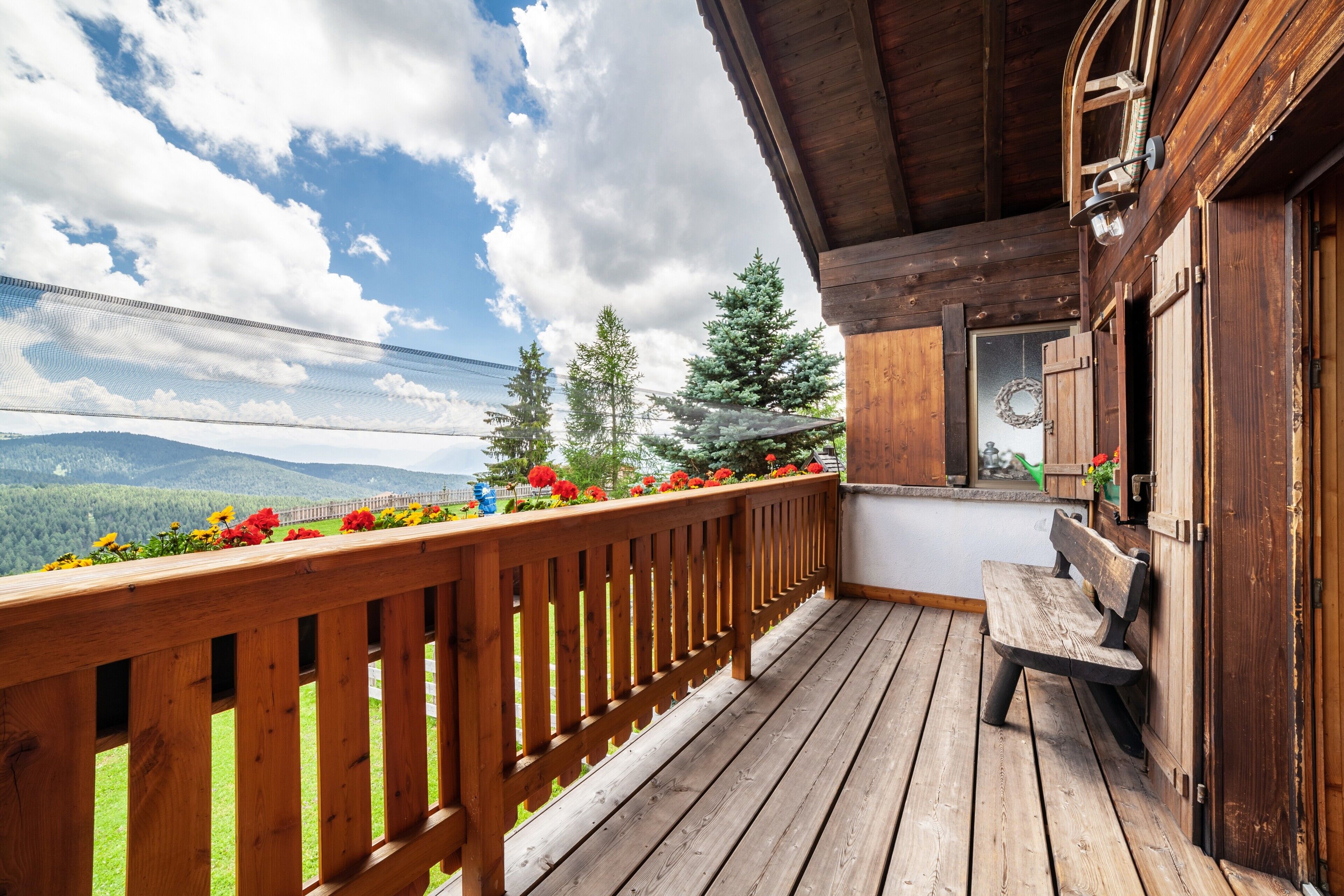 Eine Holzterrasse mit Geländer, einer Bank und Blick auf Berge.