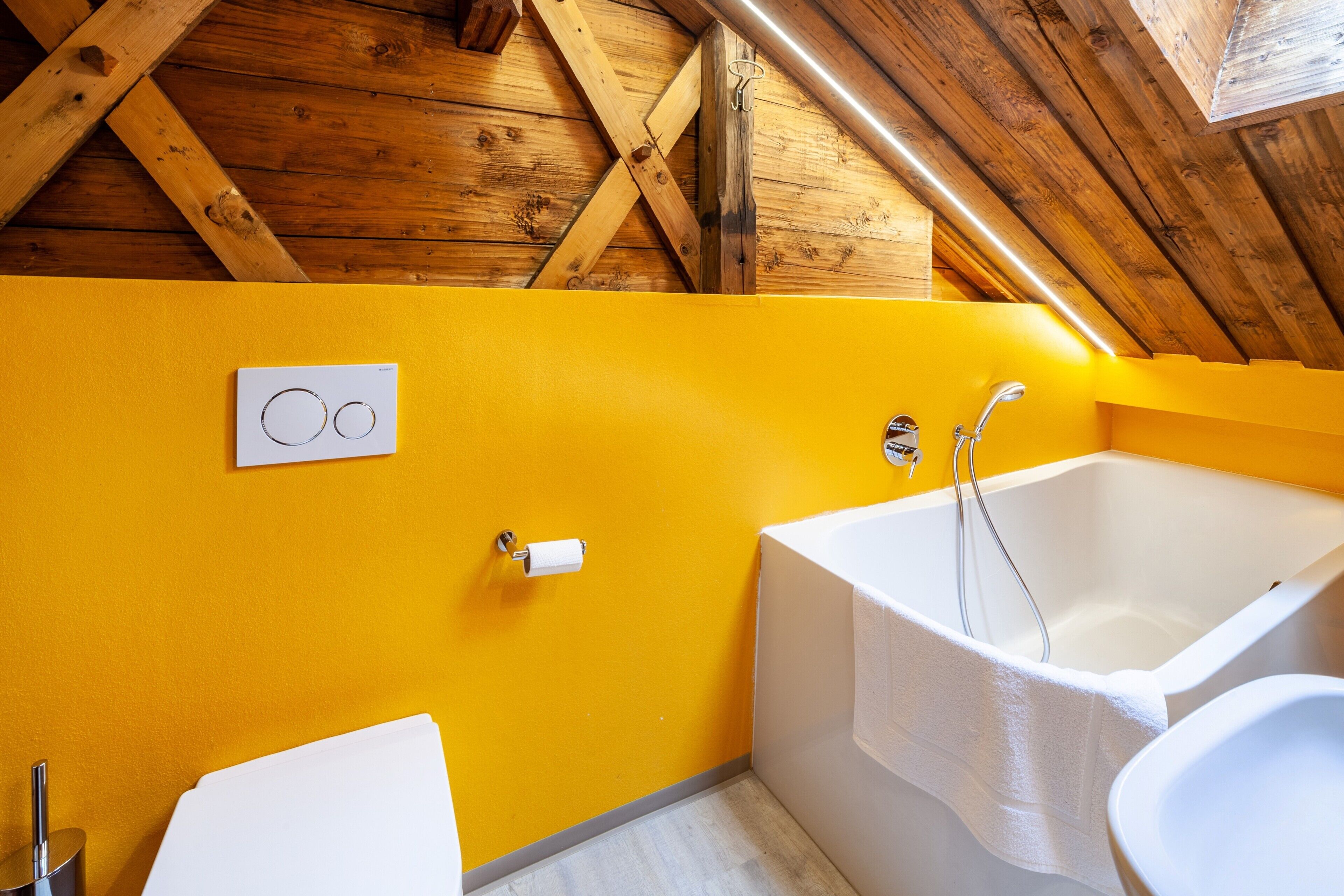 Ein Badezimmer mit Holzboden, einer gelben Wand, einer Badewanne, einem Waschbecken und einer Toilette.