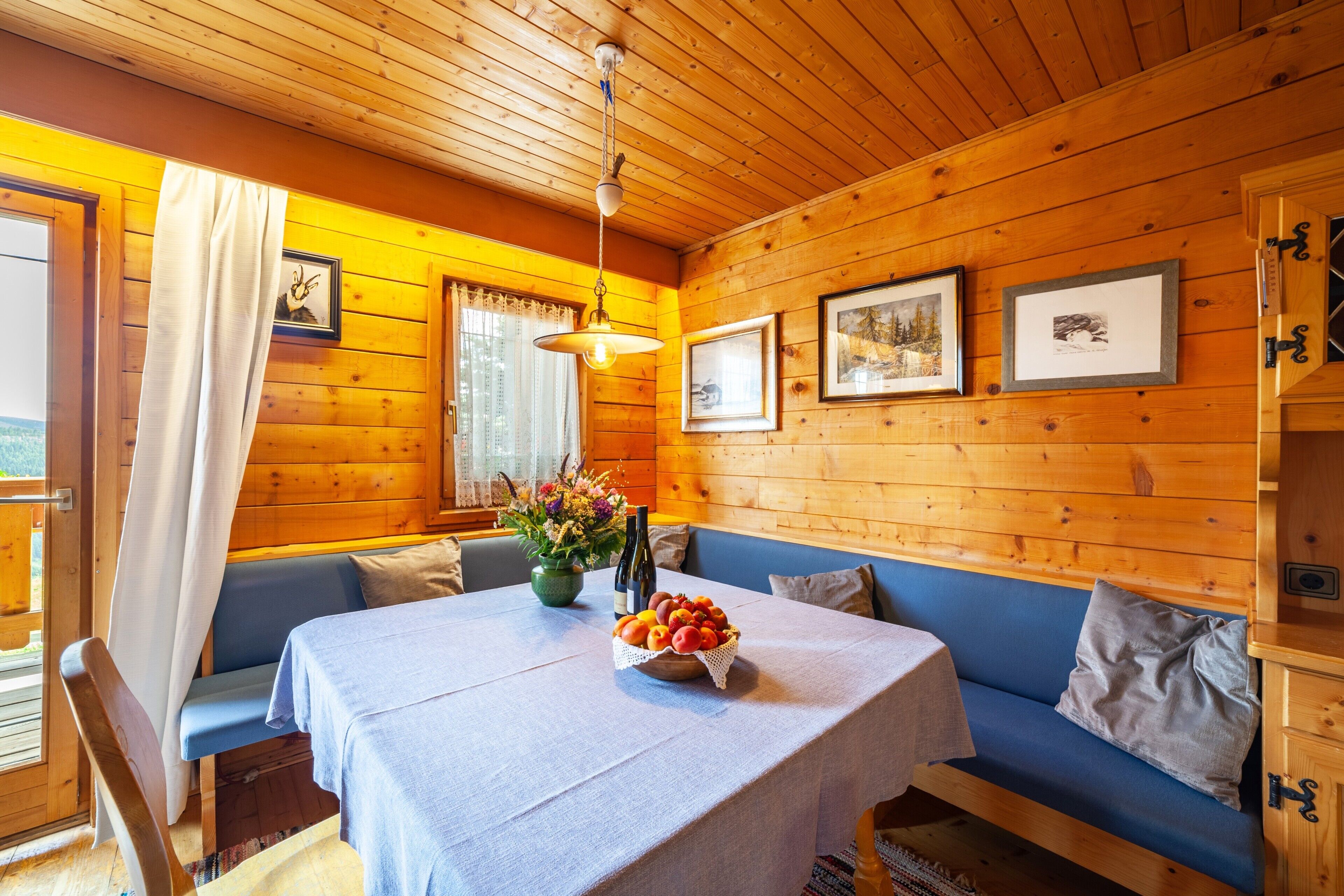 Ein Holzhütten-Innenraum mit Esstisch, blauem Sofa und gerahmten Bildern an der Wand.