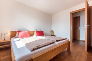 Une chambre à coucher avec un lit en bois, une table de chevet, une commode et une porte donnant sur une autre pièce.