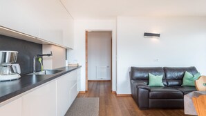 Eine moderne Küche mit Einbauherd, Spüle und Kaffeemaschine. Ein Wohnbereich mit Holzboden und einem dunkelbraunen Ledersofa mit grünen Kissen.