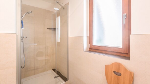 Une douche avec une porte en verre, des toilettes en bois et une fenêtre avec un cadre en bois.