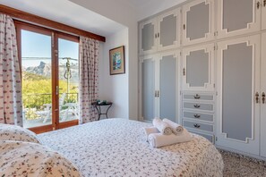Un dormitorio con cama, armario, balcón con mesa y sillas, y vistas a la montaña.