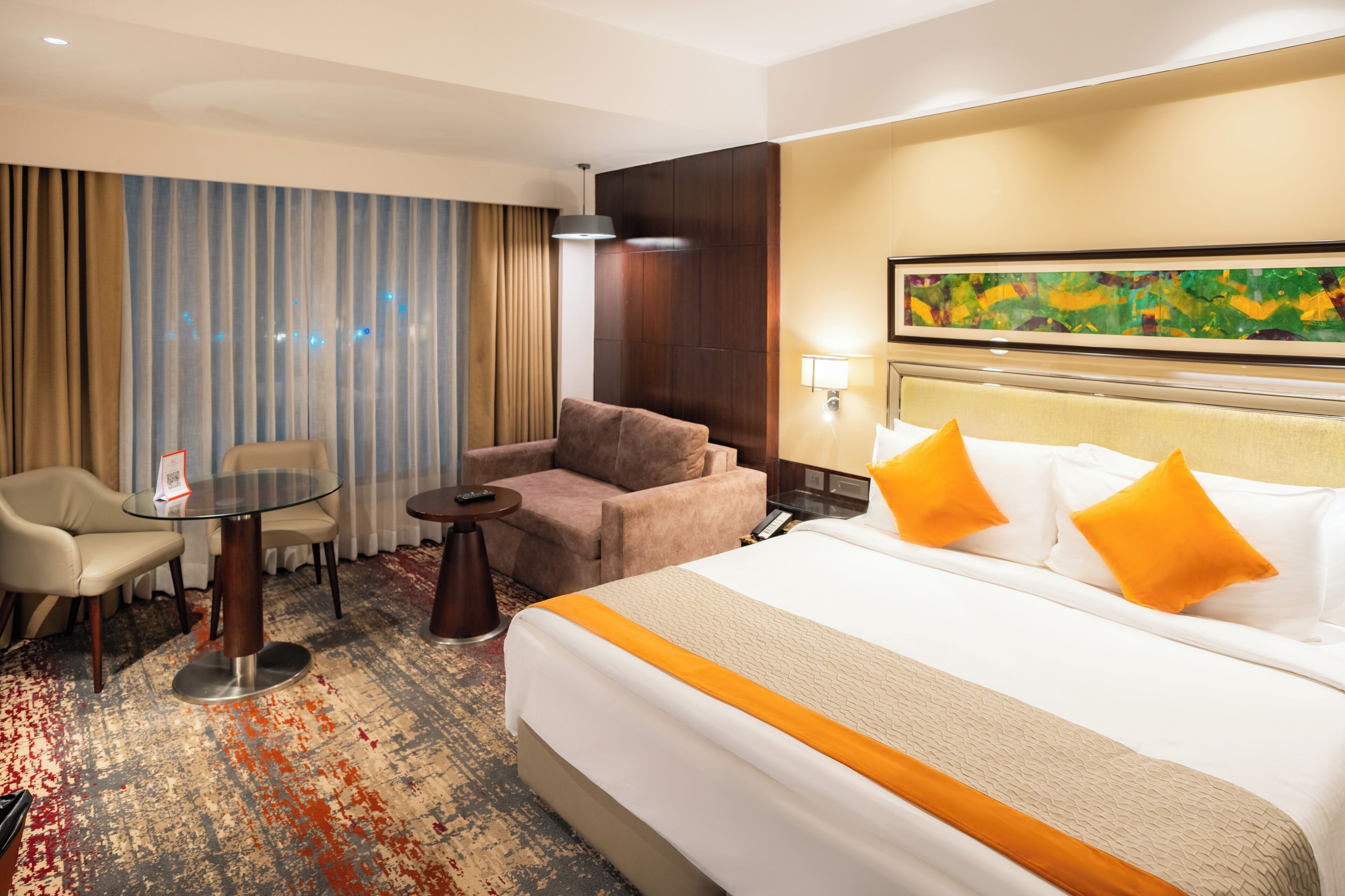 A hotel room with a large bed, a sofa, a small table, and a chair.