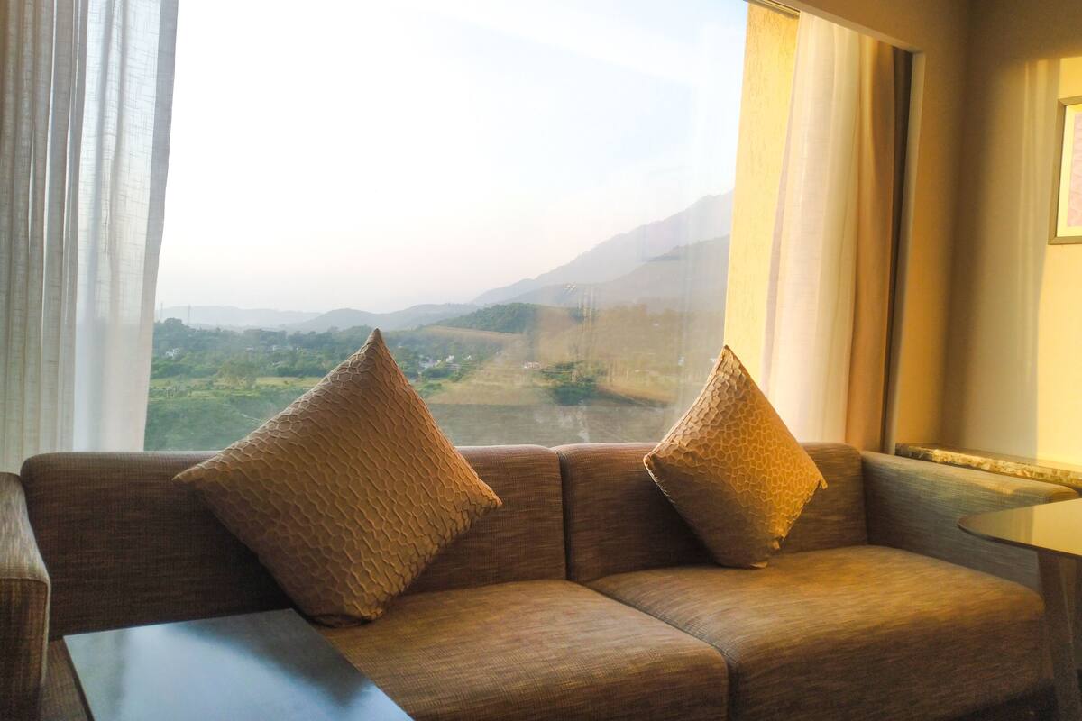Quarto com sofá e mesa, uma janela grande com vista para uma paisagem.