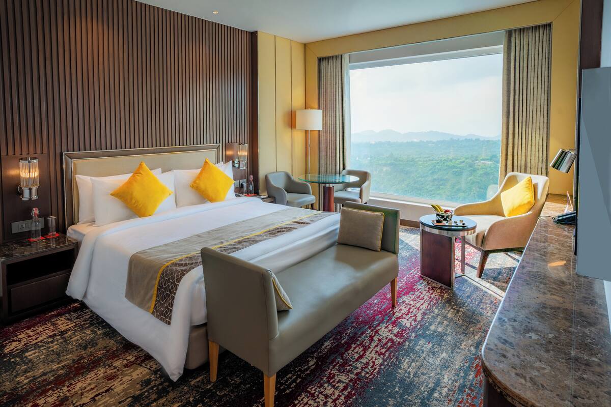 Quarto de hotel com uma cama grande, duas poltronas, uma pequena mesa e vista para as montanhas.