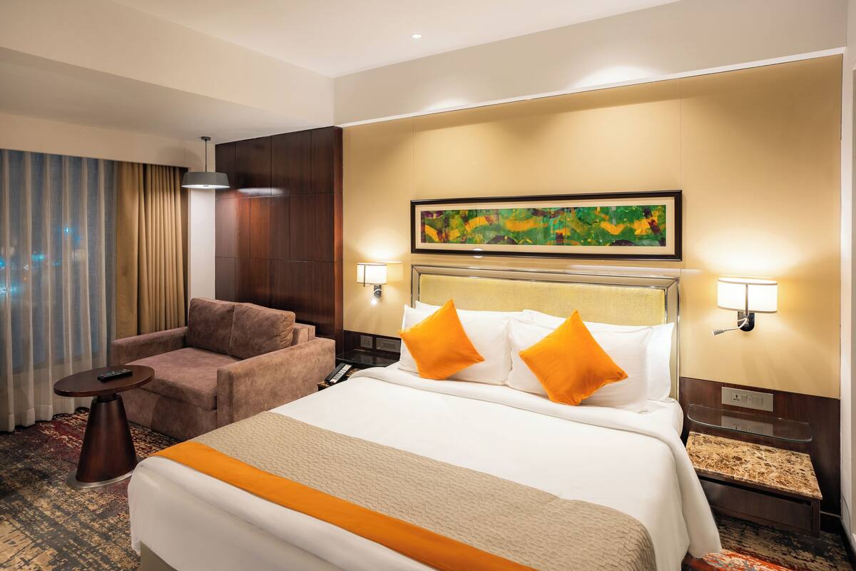Quarto de hotel com uma cama grande, um sofá, uma escrivaninha e uma pintura na parede.