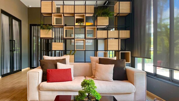 A modern living room with a sofa, coffee table, and a plant. There is a large window with curtains and a view of the outdoors. - bliQ Hotel Chanthaburi (Chanthaburi)