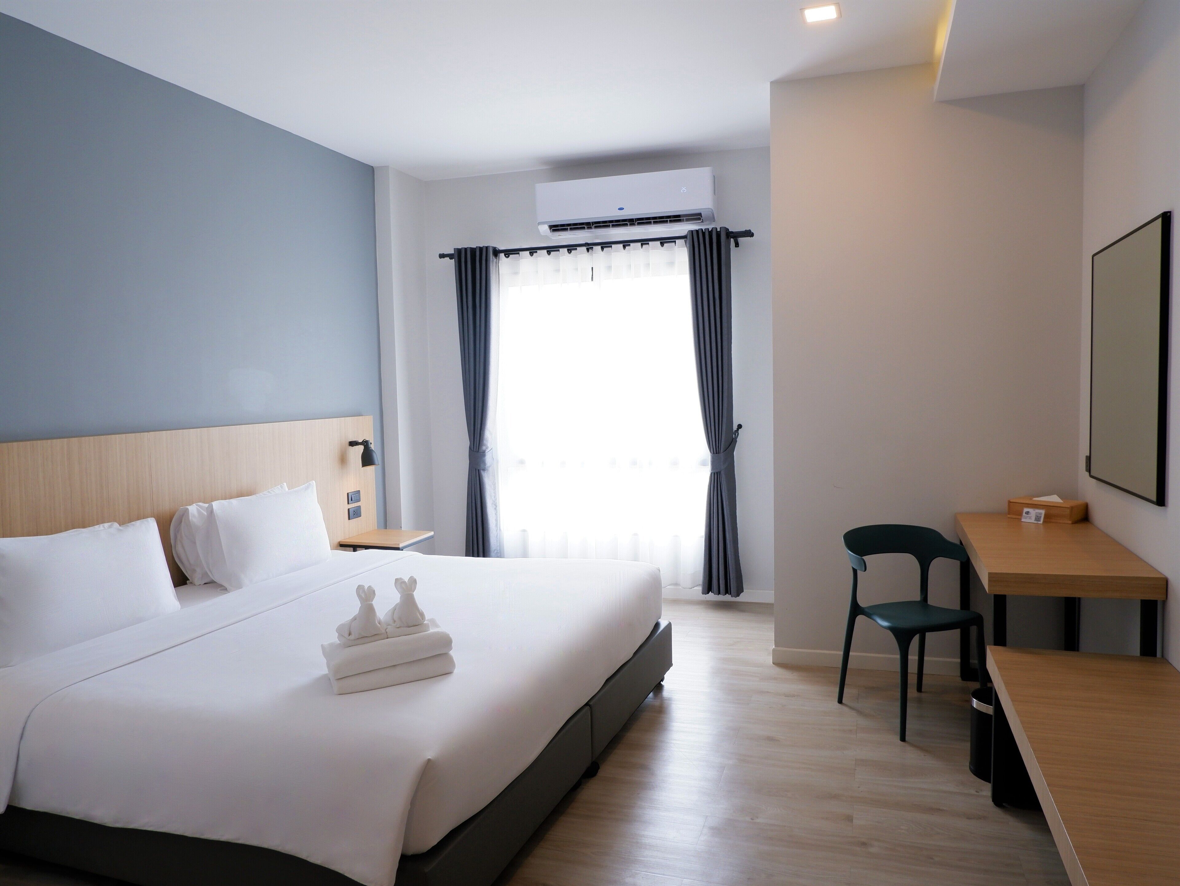 Habitación de hotel con una cama grande, un escritorio, una silla y un ventanal con cortinas.