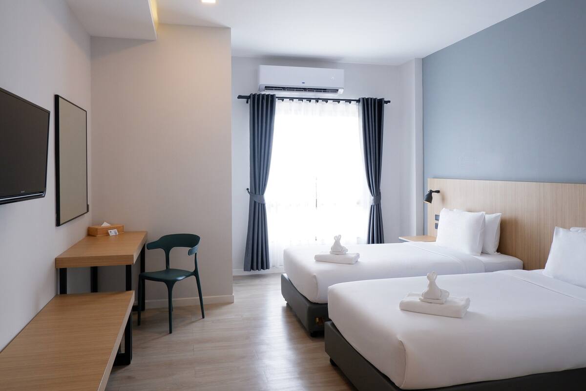 A hotel room with two beds, a desk, a chair, and a window with curtains.