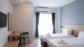 A hotel room with two beds, a desk, a chair, and a window with curtains.