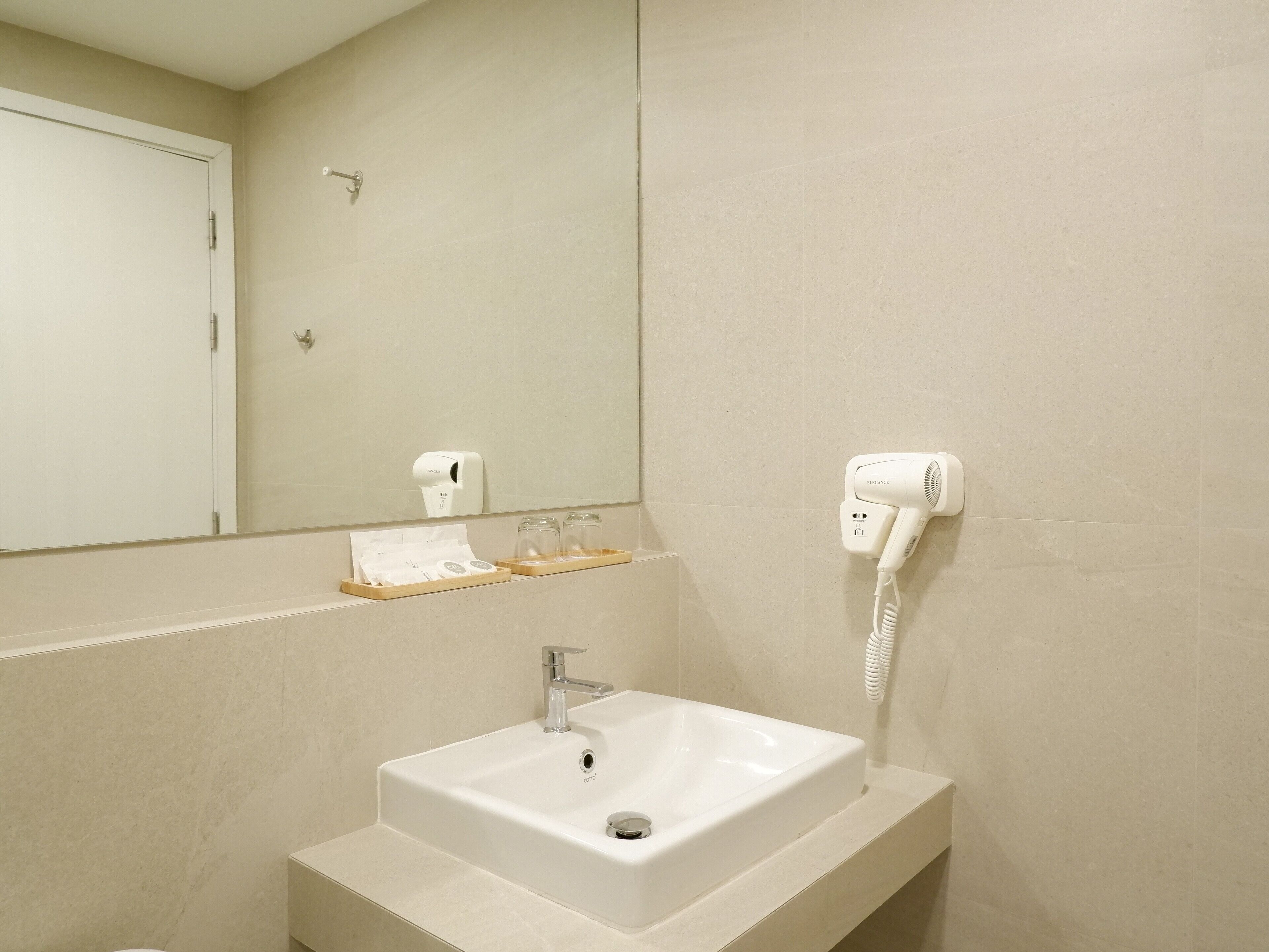 A bathroom with a white sink, a mirror, a towel dispenser, and a hairdryer mounted on the wall.