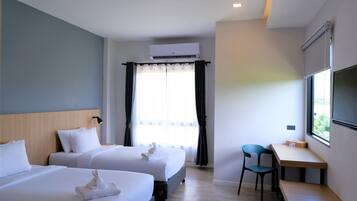 A hotel room with two beds, a desk, a chair, an air conditioning unit, and a window with curtains.