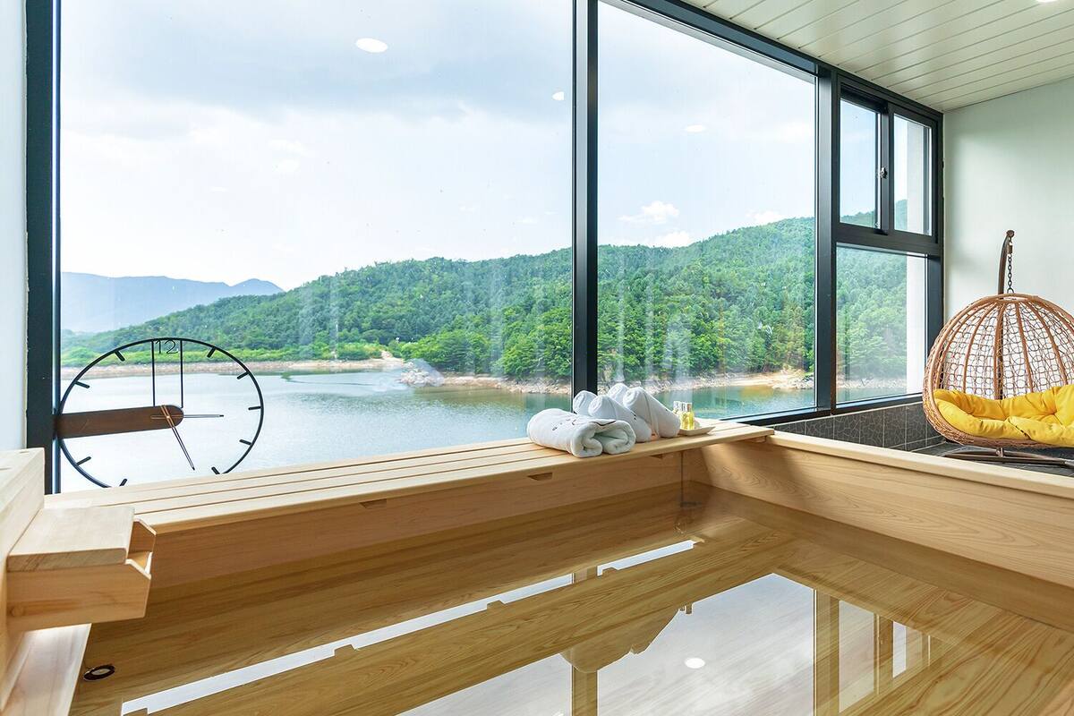 A modern room with a large window, wooden flooring, a hanging chair, and a wooden bench.