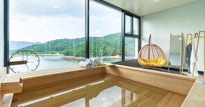 Een moderne kamer met een groot raam, houten vloer, een hangstoel en een houten bank.