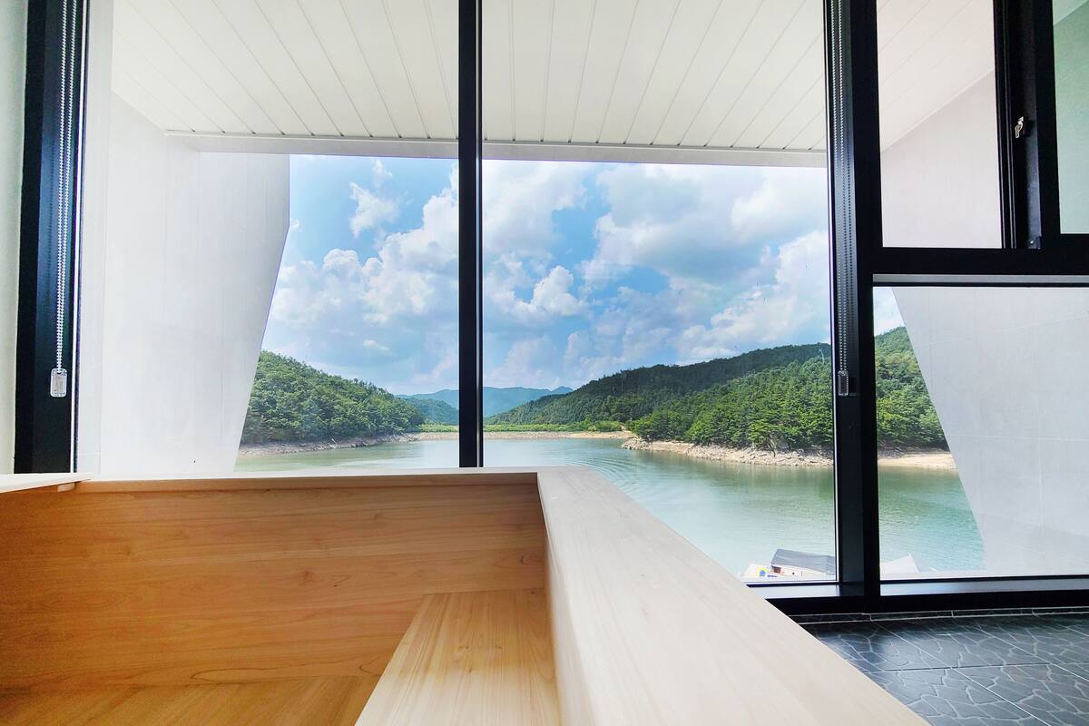 A room with a large window overlooking a river and hills.