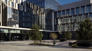 A modern building with a glass facade, a clear sky, and a landscaped courtyard with trees and seating areas. - Holiday Inn - the niu, Hub Dusseldorf Messe by IHG (Düsseldorf)