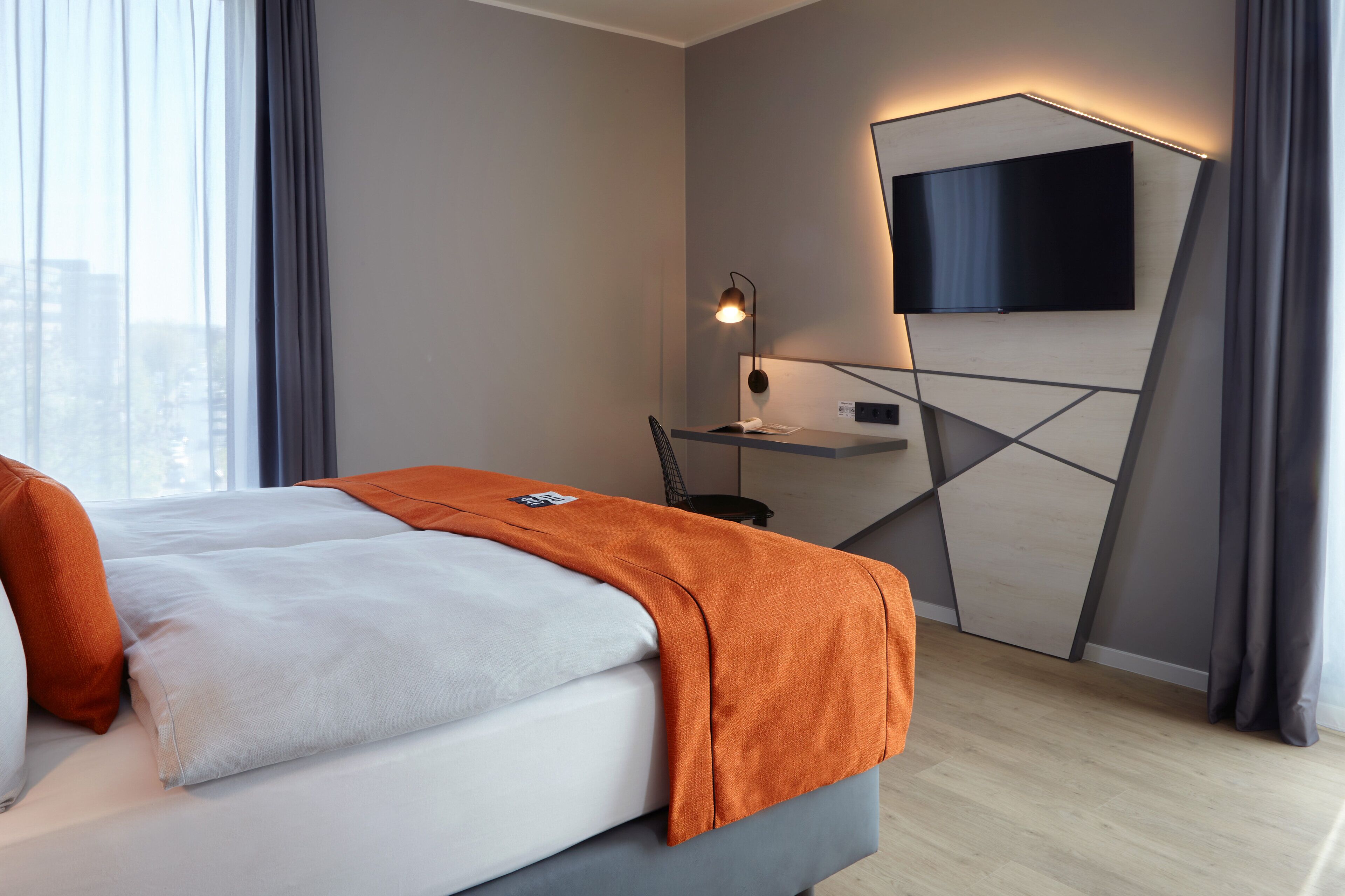 Una habitación de hotel moderna con cama, escritorio, televisor de pantalla plana y vista a la ciudad.