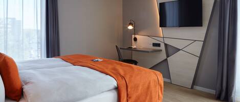 Une chambre d’hôtel moderne équipée d’un lit, d’un bureau, d’une télévision à écran plat et offrant une vue sur la ville.