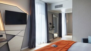 A modern hotel room with a flat-screen TV mounted on the wall, a bed with an orange throw, and a large mirror reflecting the room. - Holiday Inn - the niu, Hub Dusseldorf Messe by IHG (Düsseldorf)