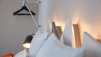 Un dormitorio ordenado con una lámpara colgante, una cama con almohadas blancas y una pared con estampado geométrico.