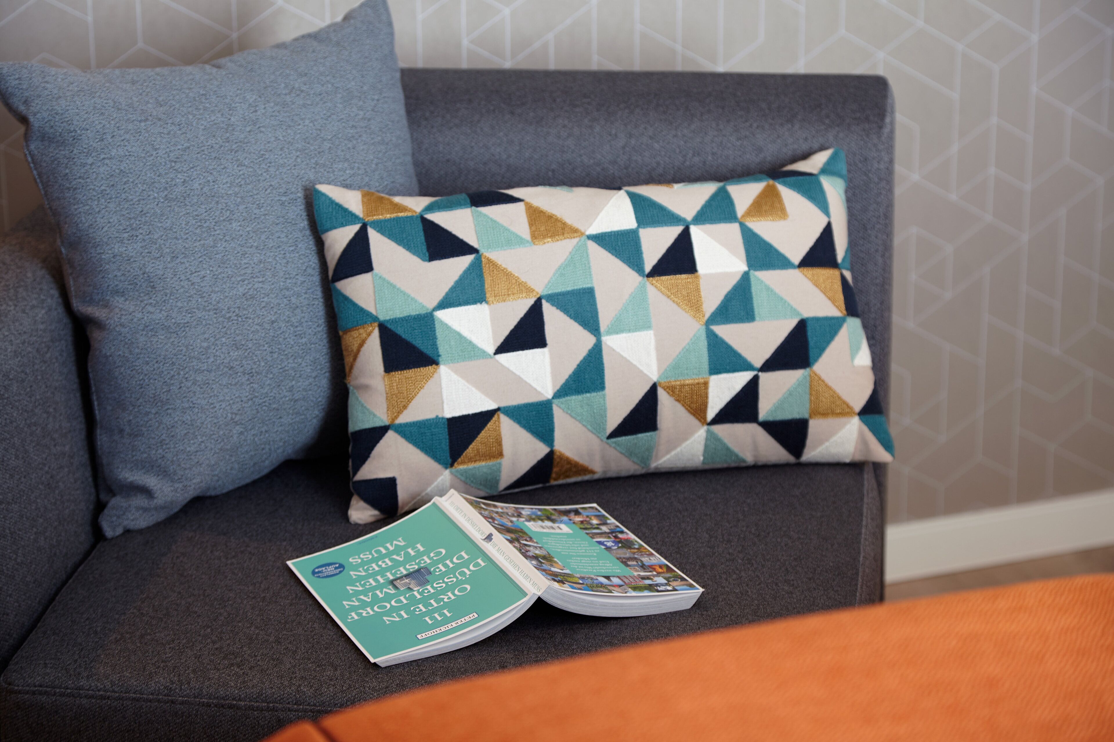 A grey sofa with a patterned pillow and a magazine on it.