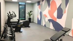 A gym with exercise equipment, a large window, and a wall with abstract art. - Holiday Inn - the niu, Hub Dusseldorf Messe by IHG (Düsseldorf)
