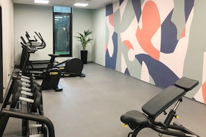 Un gimnasio con equipo de ejercicio, un ventanal grande y una pared con arte abstracto.