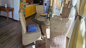 Ein gemütliches, helles Zimmer mit Korbmöbeln, einem Glastisch und einem Kühlschrank.
