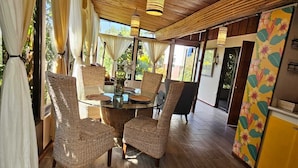 Ein Essbereich mit Korbstühlen, einem Tisch mit Glasplatte und einer Holzbalkendecke.