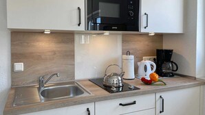 A modern kitchen with a built-in microwave, a kettle, a coffee maker, and a sink.