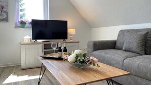 Ein modernes Wohnzimmer mit Flachbildfernseher, grauem Sofa und Couchtisch mit einer Auswahl an Weinflaschen und Gläsern.