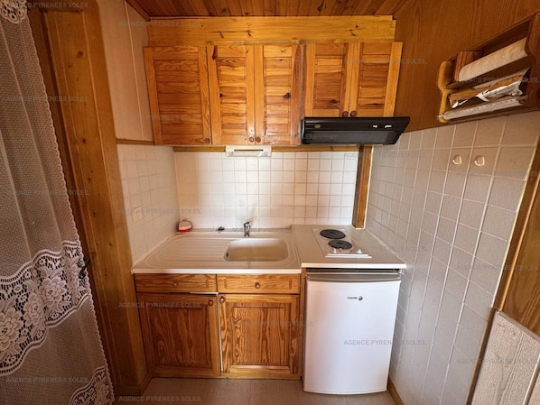 Eine kleine Küche mit Holzausstattung, einem weißen Spülbecken und einem weißen Kühlschrank.