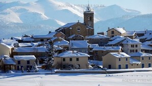 Un village enneigé, avec des bâtiments traditionnels, une église et une chaîne de montagnes en arrière-plan.