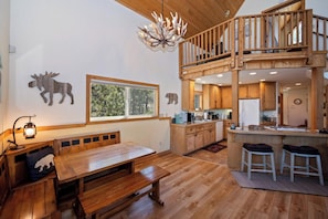 A spacious kitchen with wooden cabinets, a dining area with a bench, and a loft bedroom with a balcony. - Beautiful Boulder Bay Setting & Lake Views! Game Room! HOT TUB! (Big Bear Lake)