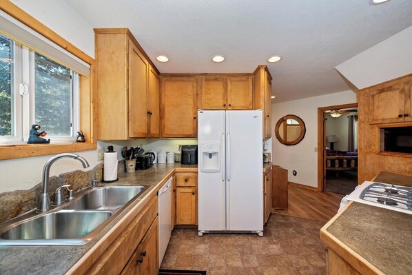 A kitchen with wooden cabinets, a white refrigerator, a sink, and a window with a view of trees.