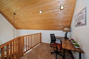 Un plafond en bois avec des luminaires suspendus, un escalier en bois, un bureau avec une chaise et un panneau fixé au mur.