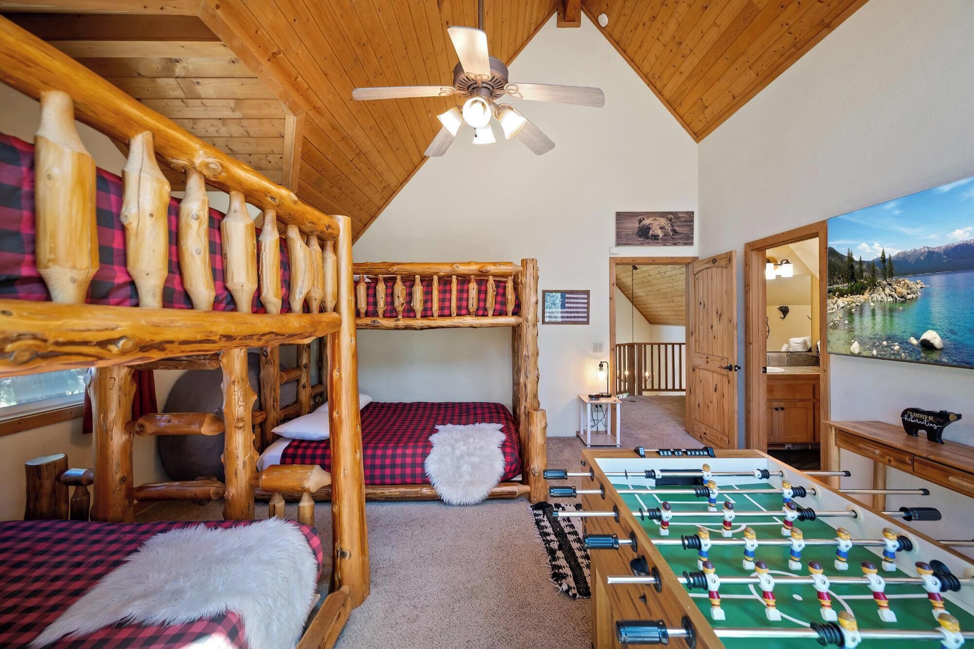 A cozy room with a wooden bunk bed, a ceiling fan, a foosball table, and a large window overlooking a lake.