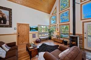 Ein gemütliches Wohnzimmer mit Kamin, Holzmöbeln und großen Fenstern mit Blick ins Freie.
