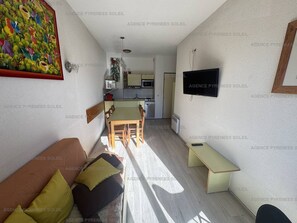 A compact living space with a kitchenette, a dining area, and a TV mounted on the wall.