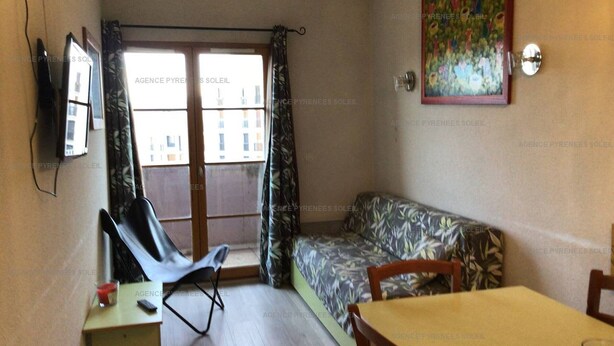 A small, furnished room with a sofa, a table, and a TV.