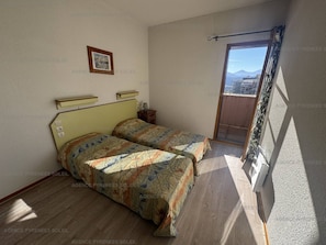 Un dormitorio con dos camas, una mesita de noche pequeña, un cuadro enmarcado en la pared y un balcón con vistas.
