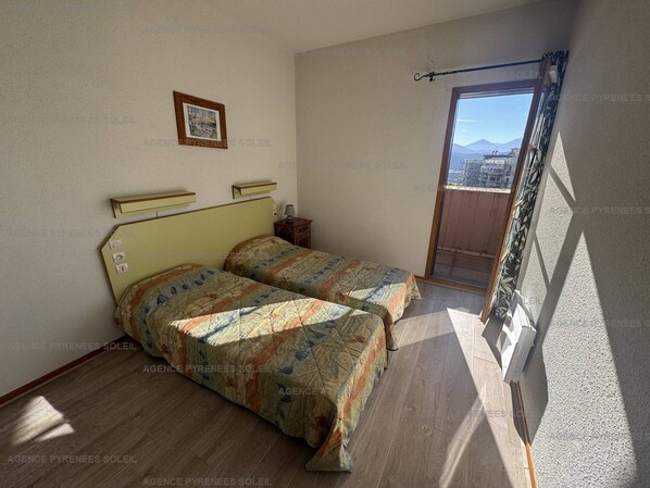 A bedroom with two beds, a small bedside table, a framed picture on the wall, and a balcony with a view.