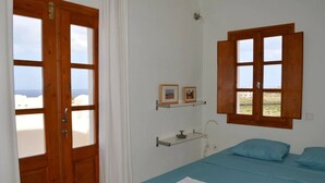 A bedroom with a bed, a wooden door, a window, and a shelf with pictures.