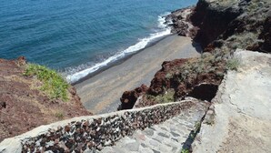 A coastal landscape with a rocky shoreline, a sandy beach, and a stone staircase leading down to the beach.