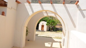 Un portail en arc donne accès à une cour intérieure où se trouve un petit bâtiment, entouré de murs blancs et de poutres en bois.