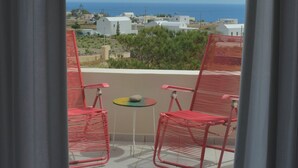 Un balcon avec deux chaises rouges et une petite table, donnant sur une zone côtière avec des bâtiments et la mer.