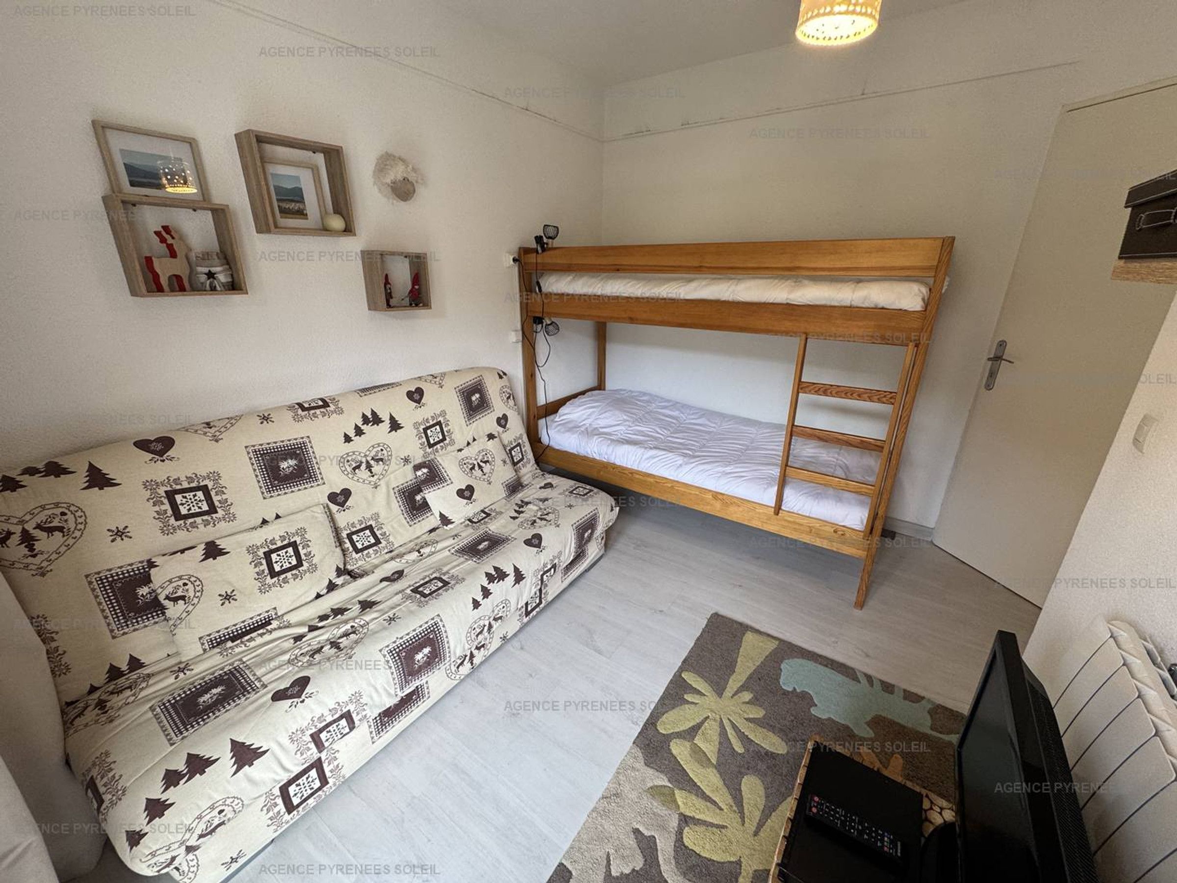 Una habitación pequeña con una cama nido, un sofá estampado y un televisor.