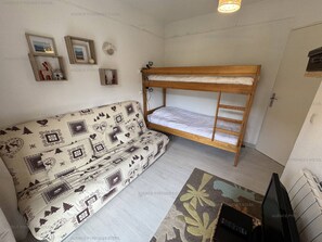 A compact room with a bunk bed, a patterned sofa, and a television.