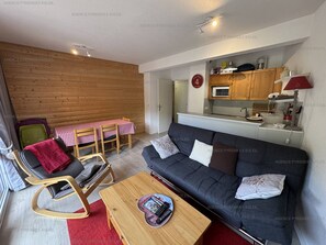 A compact living space with a sofa, a small dining table, a kitchenette, and a wooden wall.